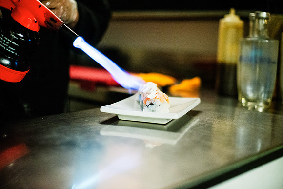 Chef uses torch to prepare gourmet sushi in a restaurant kitchen